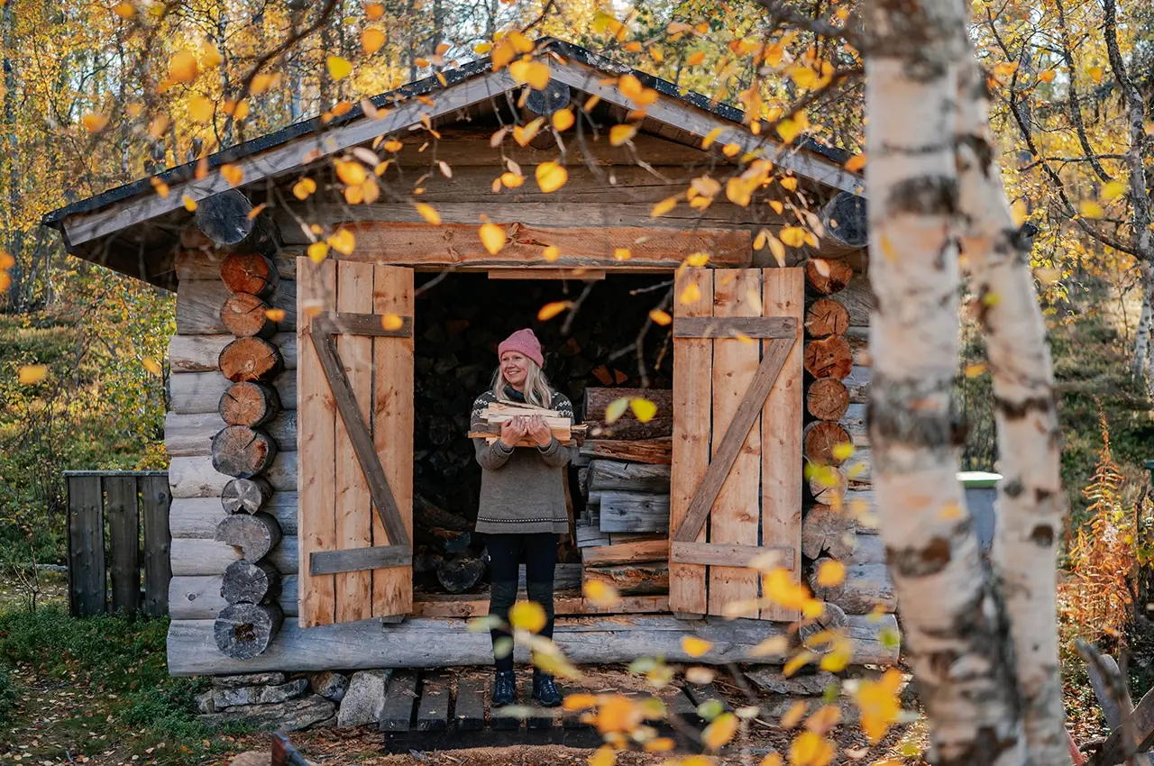 woman carrying firewood in her arms outside a small shed