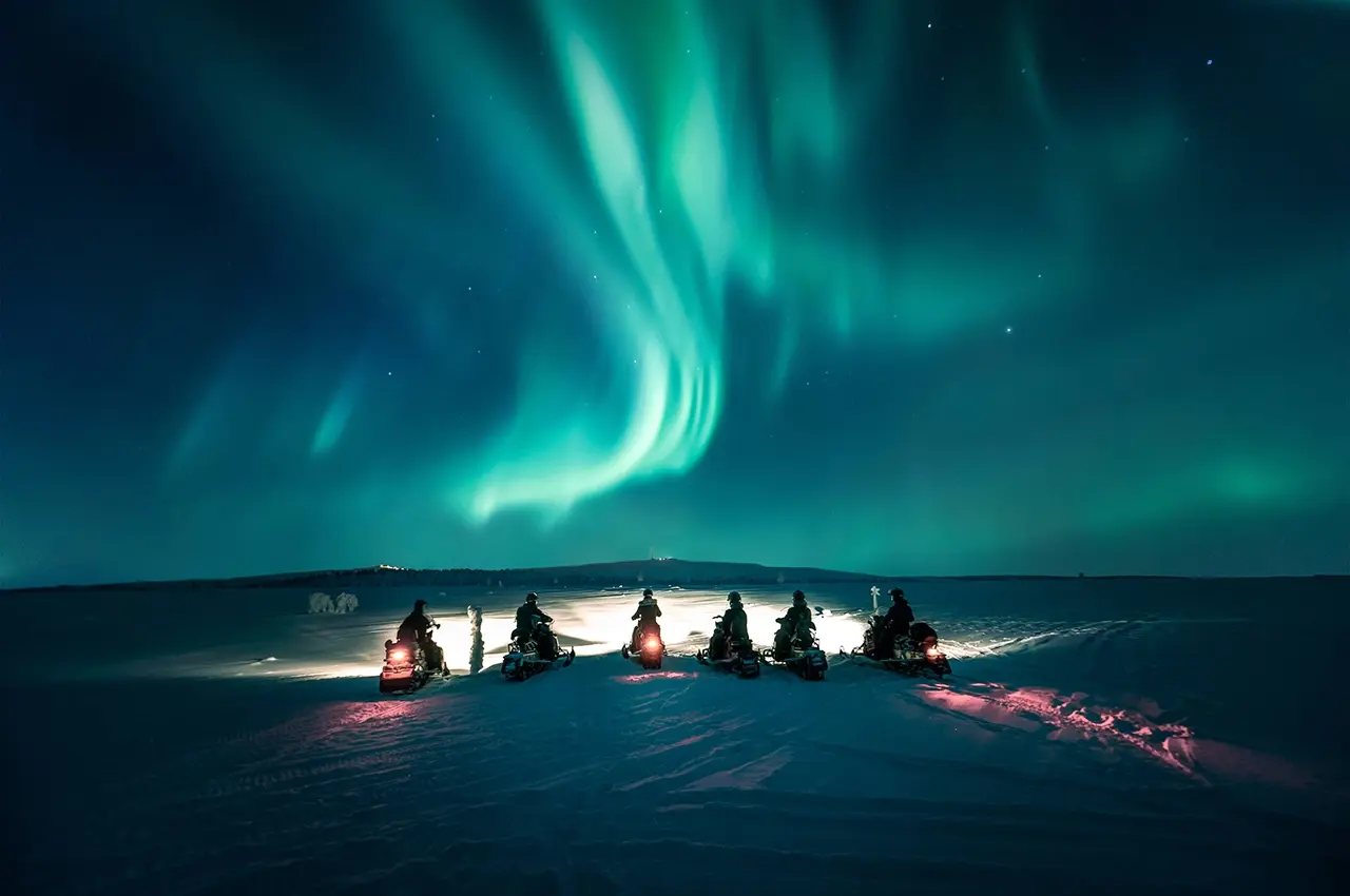 AuroraVillage snow mobiles in a row with the northern light, aurora borealis, in the sky at Aurora Village